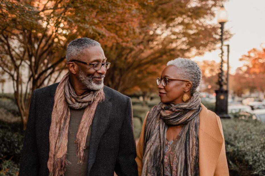 A stylish Black couple aged 55 to 60 walking hand in hand through an upscale city park at golden hour.