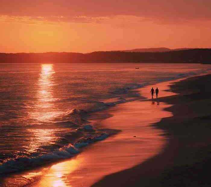 Couple walking along a beach at sunset with golden light reflecting on the ocean, creating a calm and romantic atmosphere
