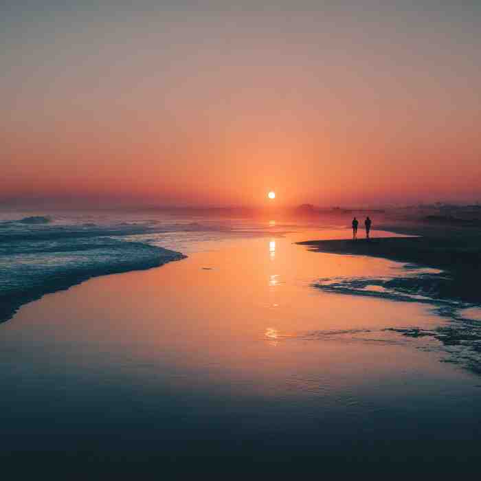Couple walking along the beach at sunset with warm golden light reflecting on the water
