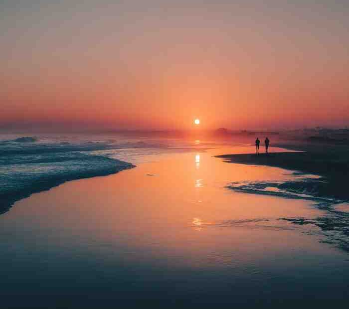 Couple walking along the beach at sunset with warm golden light reflecting on the water
